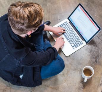 Person sitting on floor while typing on a laptop