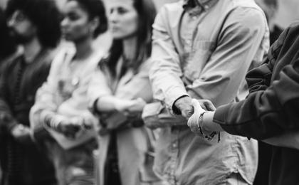 A black and white photo of a line of people with linked hands